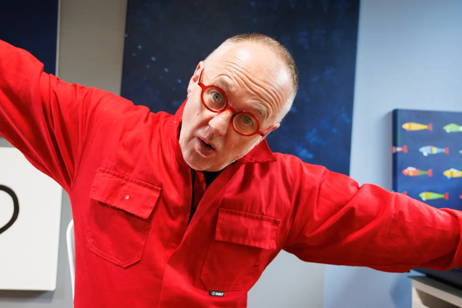 Sam Grudge in red coveralls with outstretched arms.