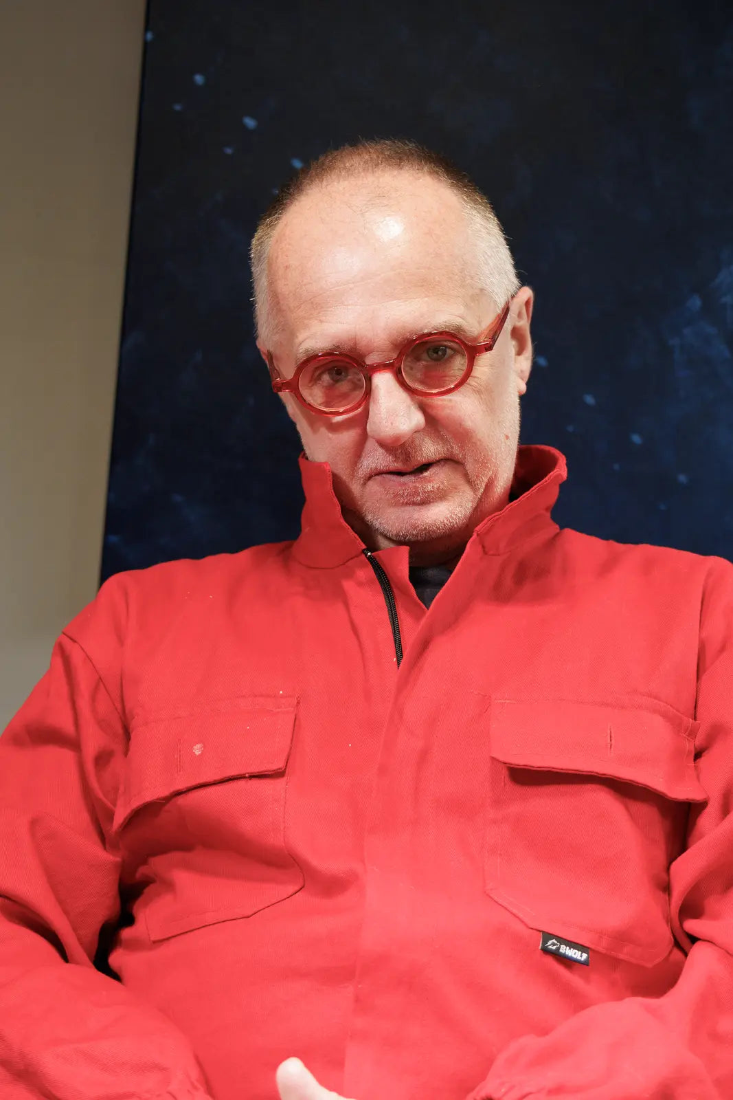 Portrait of Sam Grudge in red coveralls and round red glasses.