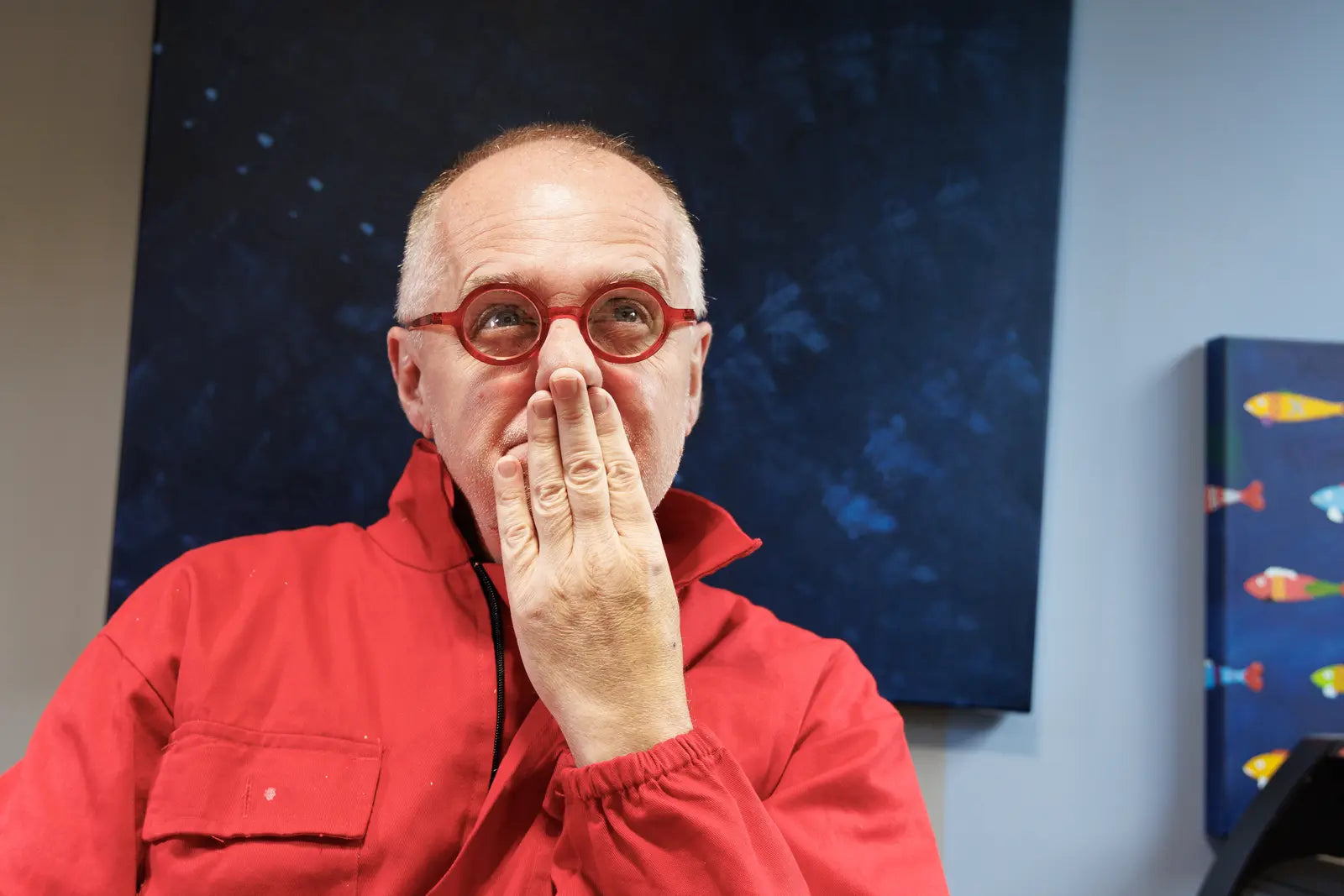 Sam Grudge in red coveralls among paintings in the studio.